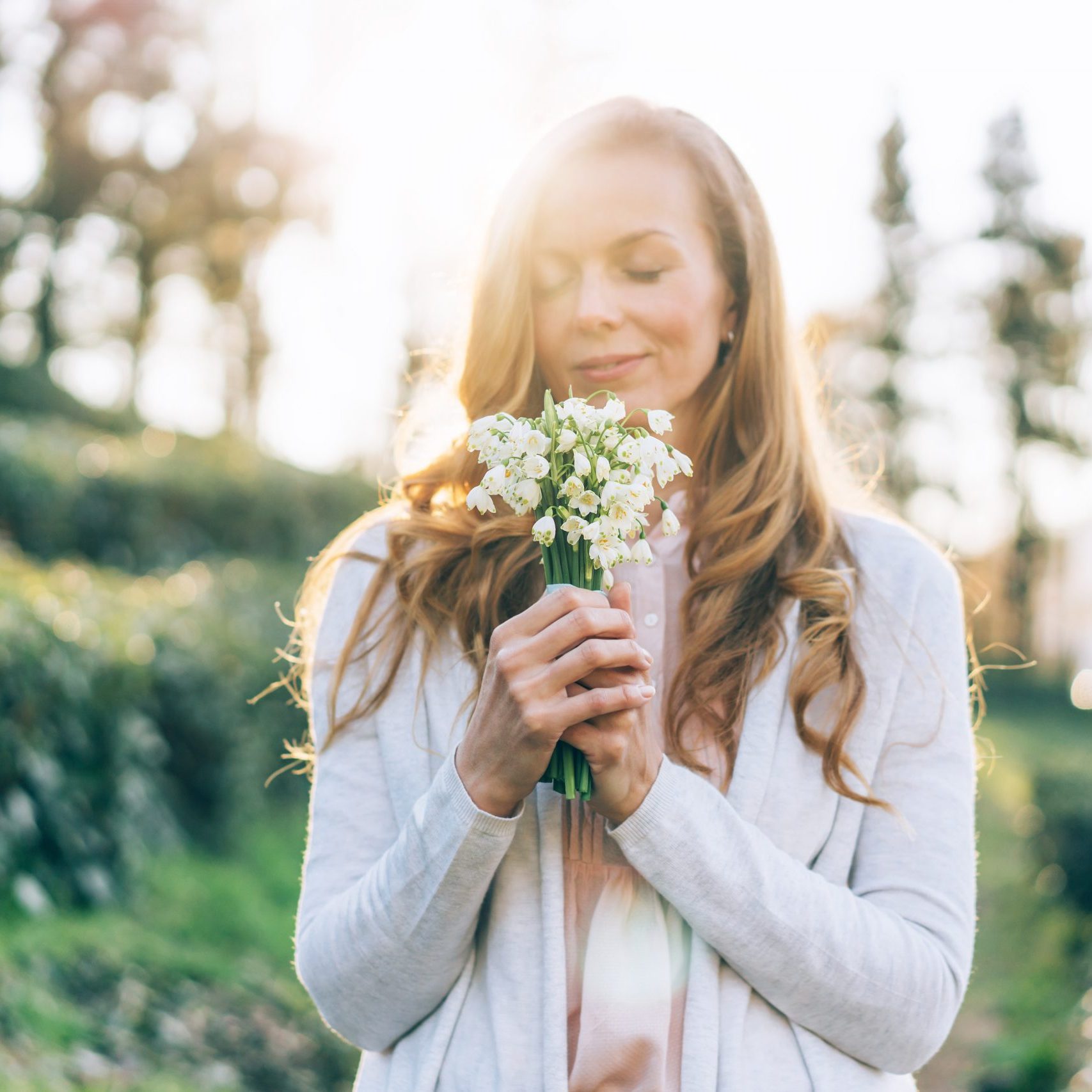 Woman in backlight smelling and showing off her beautiful snowdrops flowers bouquet. Perfect image with copy space.