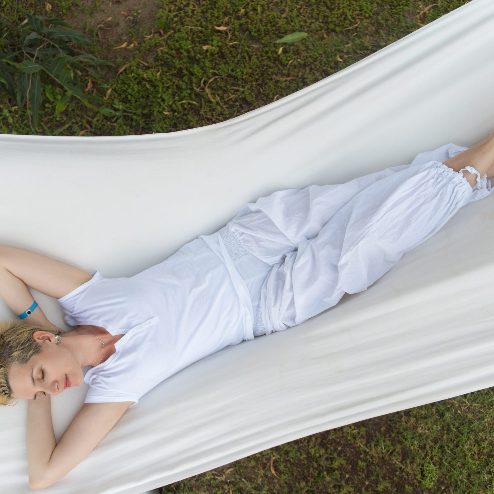 beautiful young woman enjoying free time while resting on white hammock in the backyard